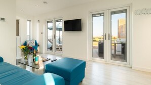 En moderne stue med en sofa, et sofabord med blomster, et fjernsyn og en skydedør til et udendørs område.