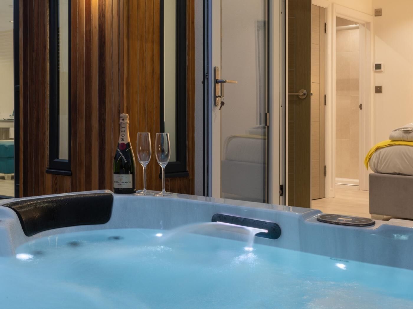 Un bain à remous avec une bouteille de champagne Moët et deux verres, un mur revêtu de panneaux en bois et une porte donnant accès à une salle de bain.