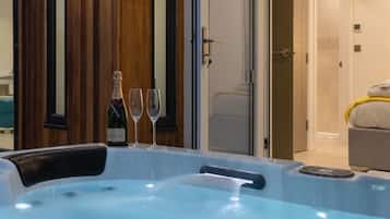 Un bain à remous avec une bouteille de champagne Moët et deux verres, un mur revêtu de panneaux en bois et une porte donnant accès à une salle de bain.