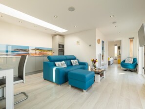 Ein modernes Wohnzimmer mit Sofa, Hocker und einem Essbereich mit Tisch und Stühlen.