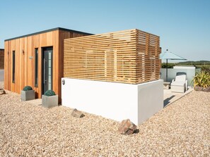 Un bâtiment moderne doté d’un mur à lattes de bois, d’une porte et d’un espace patio comprenant un fauteuil de relaxation et un parasol.