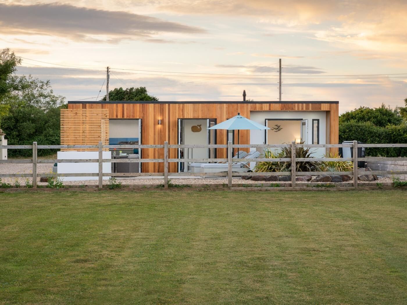 Une maison moderne avec une façade en bois, une cour clôturée et un ciel dégagé.