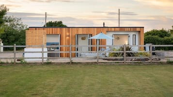 Une maison moderne avec une façade en bois, une cour clôturée et un ciel dégagé.