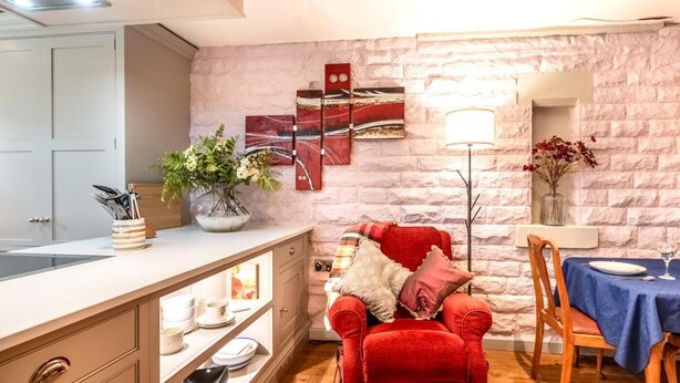 Un'accogliente sala da pranzo con una sedia rossa, un tavolo con tovaglia blu e una parete in pietra decorata con opere d'arte.
