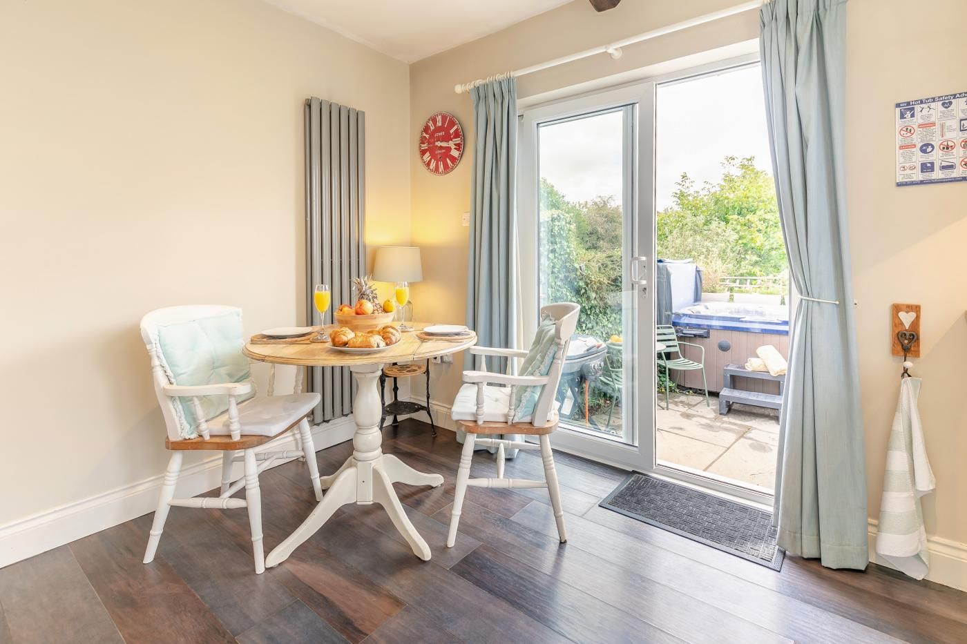 A dining area with a round table, two chairs, a clock, and a view of the outside.