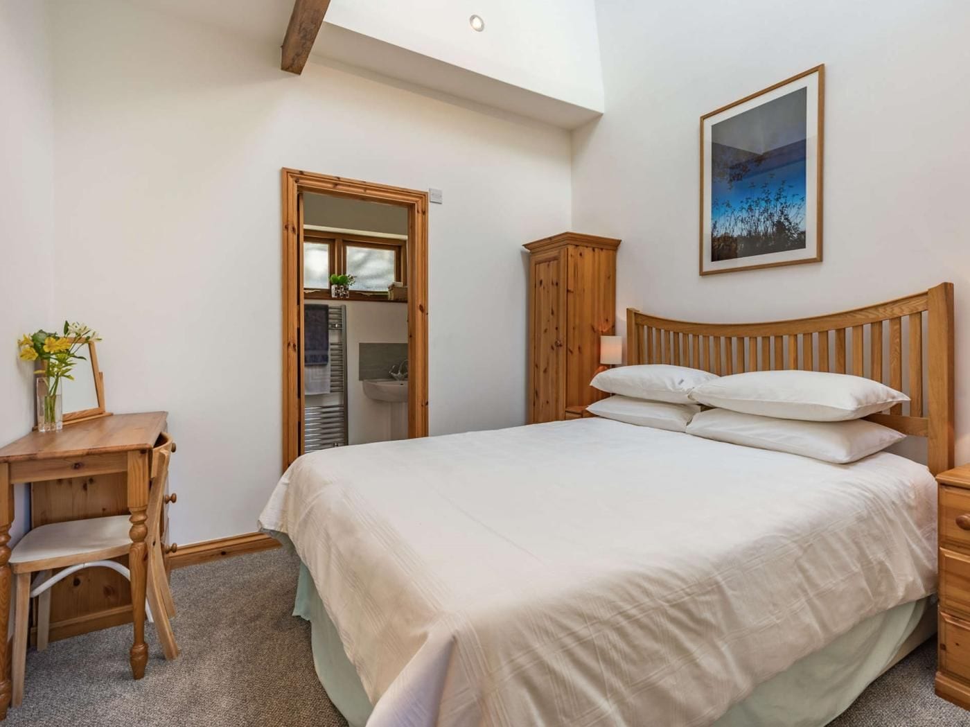 A bedroom with a wooden bed, a bedside table, a chair, a wardrobe, and a bathroom visible through an open door.