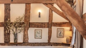 A rustic interior with exposed wooden beams, a brown leather sofa, a vase with flowers, and wall-mounted artwork. - 4 Bed in Ludlow (oc-chl22) (Orleton)
