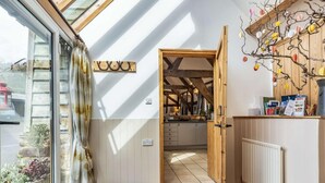 A room with a wooden floor, a black mat at the entrance, a wooden door leading to a kitchen, and a window with a curtain. - 4 Bed in Ludlow (oc-chl22) (Orleton)