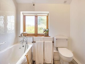 Badeværelse med badekar, toilet og vindue med udsigt til grønne omgivelser.