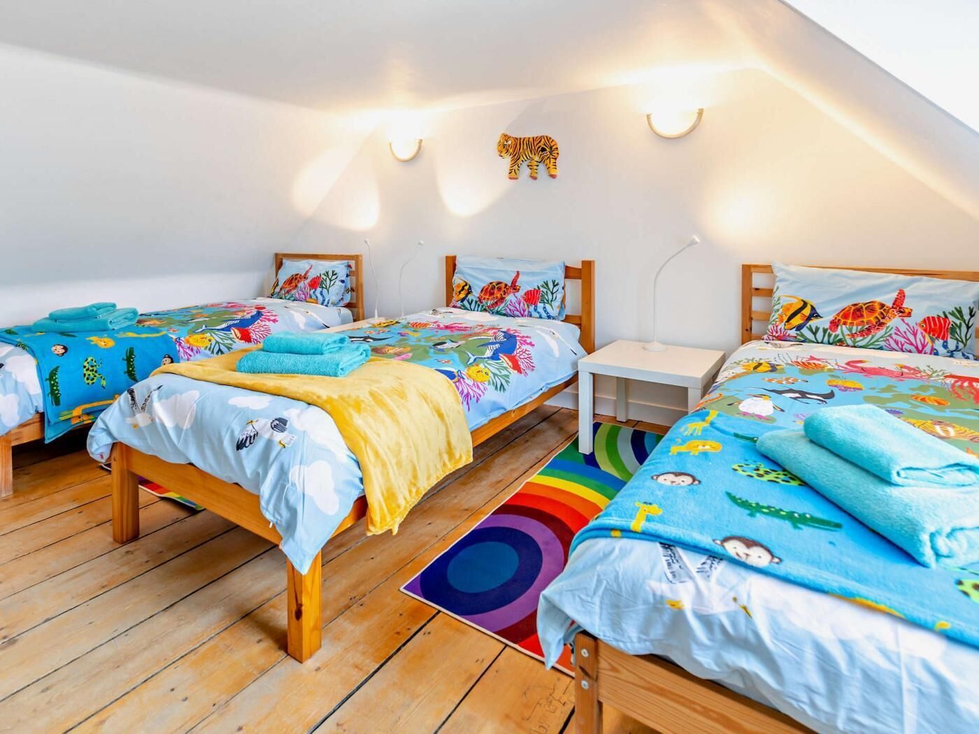 A room with two wooden beds, colorful bedding, a small white nightstand, and a ceiling light fixture.