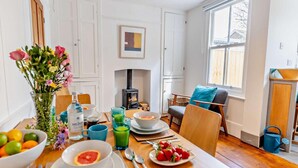 A dining area with a table set for breakfast, a fireplace, and a view of the outside. - 3 Bed in Whitstable (oc-52559) (Whitstable)