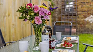 A table set for breakfast with a vase of flowers, a bottle of Hildon, and plates of food. - 3 Bed in Whitstable (oc-52559) (Whitstable)