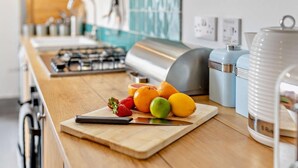 A kitchen counter with a cutting board holding fruits, a gas stove, and kitchen appliances. - 3 Bed in Whitstable (oc-52559) (Whitstable)