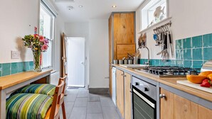 A kitchen with a stove, oven, and wooden cabinets. There is a window with a view of the outside, and a door leading to another room. - 3 Bed in Whitstable (oc-52559) (Whitstable)