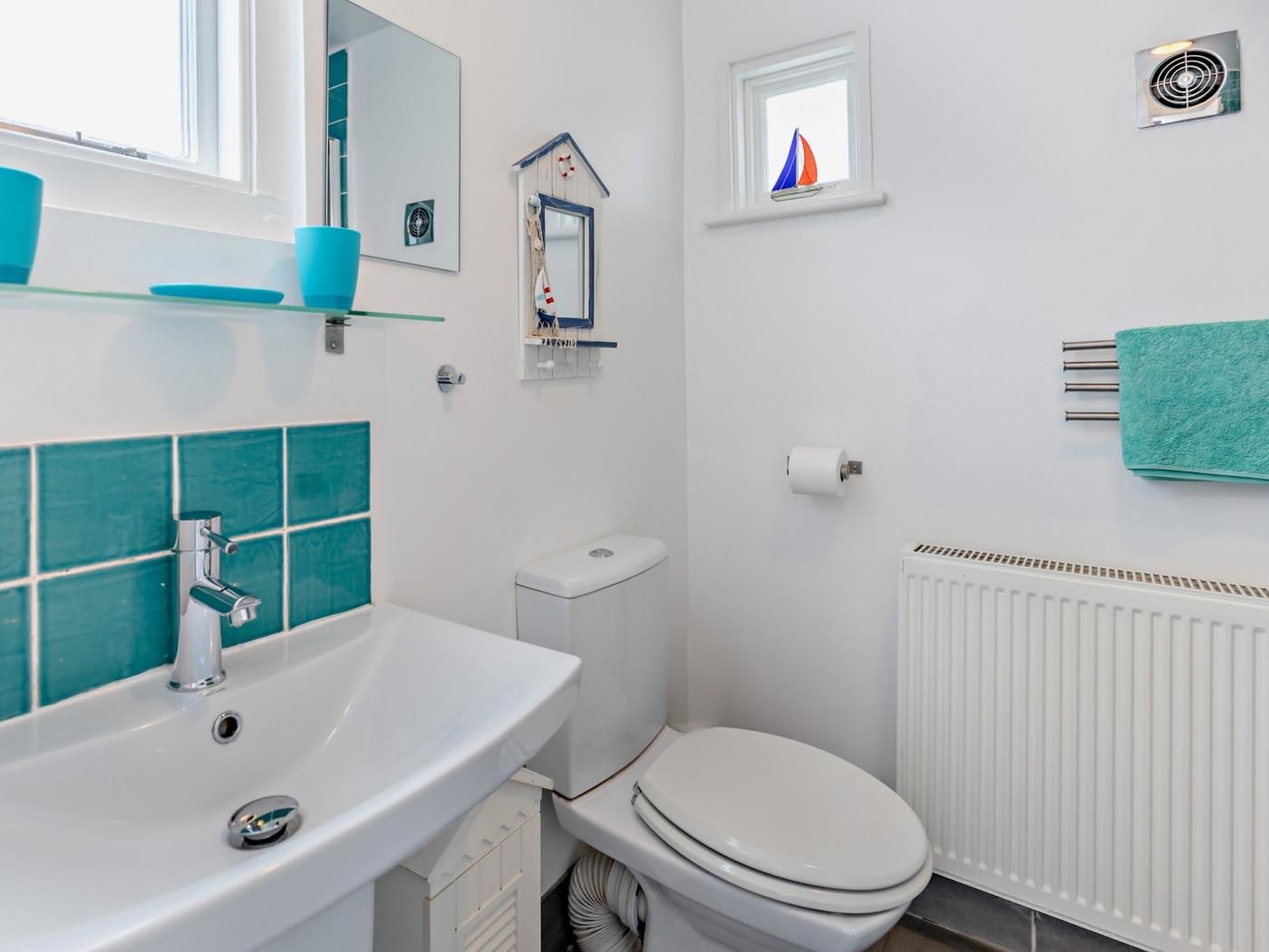 Een badkamer met een wit wastafelmeubel, een toilet, een klein raam met decoratie van een zeilboot en een handdoekhouder.