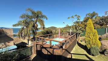 Um deck de madeira com piscina, cercado por vegetação tropical e vista para o oceano.