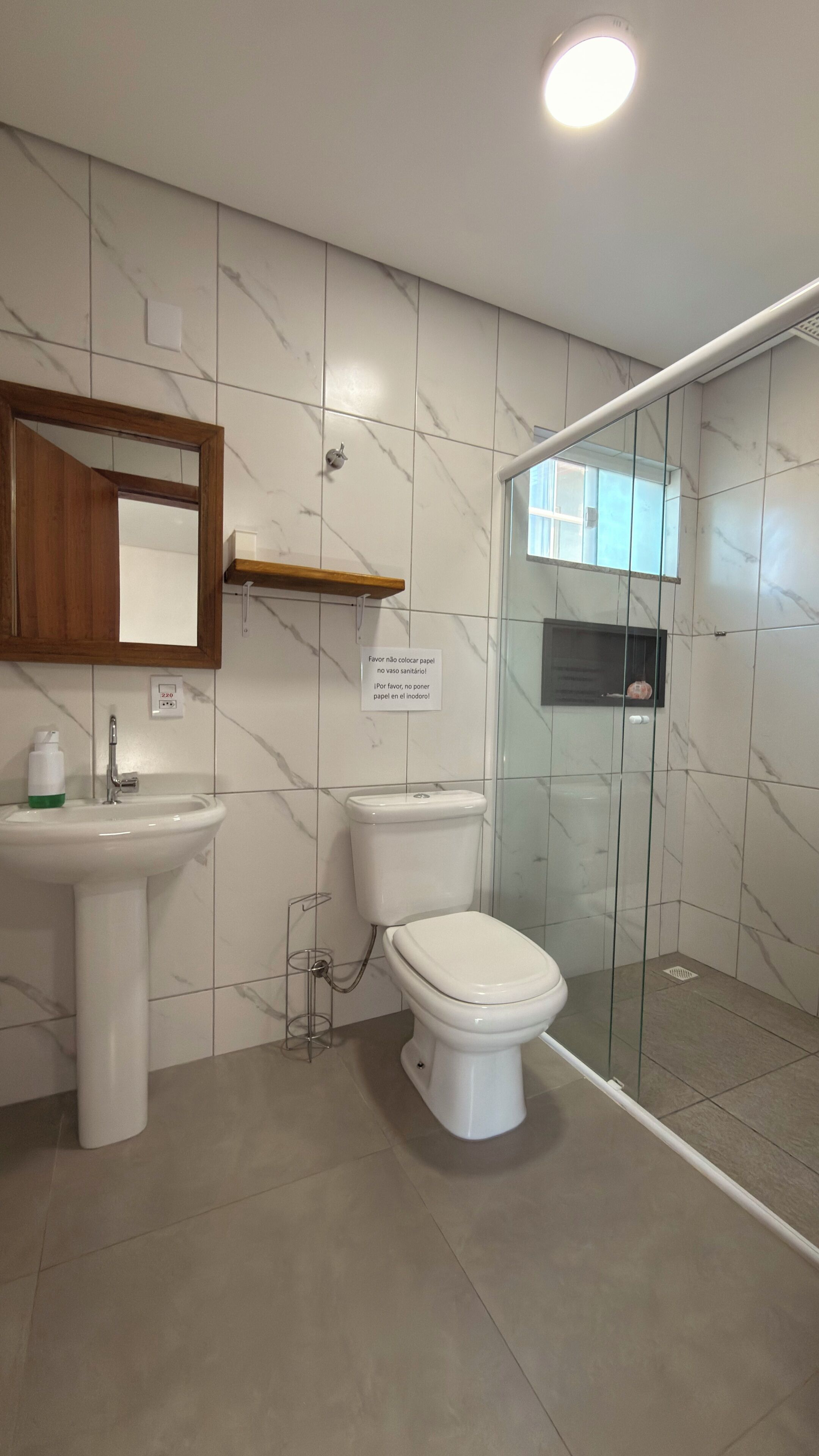 Baño con inodoro, lavamanos y cabina de ducha de vidrio.