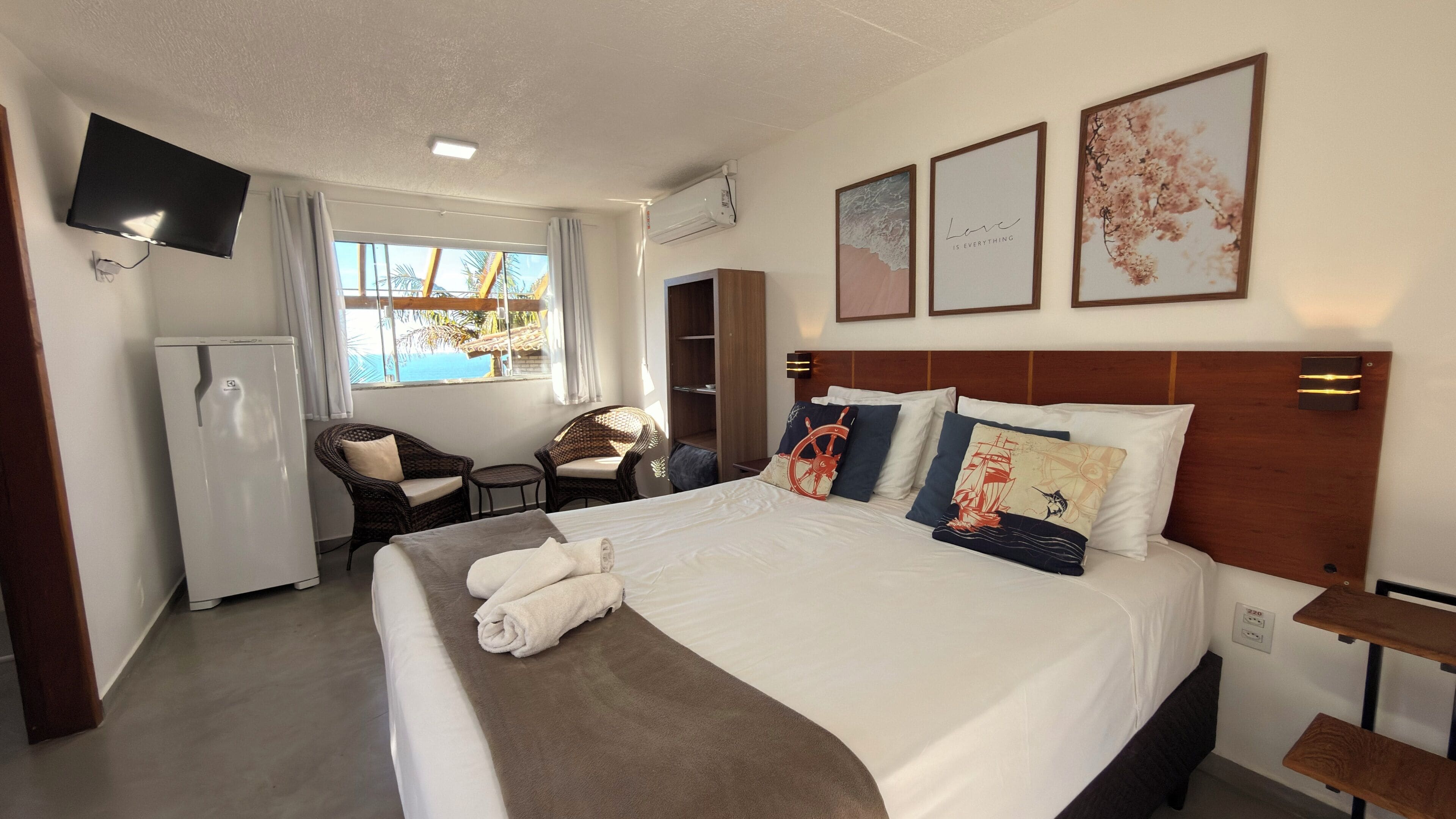 Habitación de hotel con cama, televisor, escritorio, silla, armario y ventana con vistas.