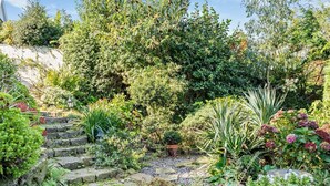 A garden with stone steps leading up to a wooden deck, surrounded by various plants and trees. - 1 Bed in Abergavenny (oc-52882) (Gilwern)
