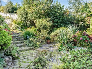 A garden with stone steps leading up to a wooden deck, surrounded by various plants and trees. - 1 Bed in Abergavenny (oc-52882) (Gilwern)