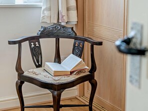 A wooden chair with a lace doily, a book, and a curtain in a room with a wooden door and a window.