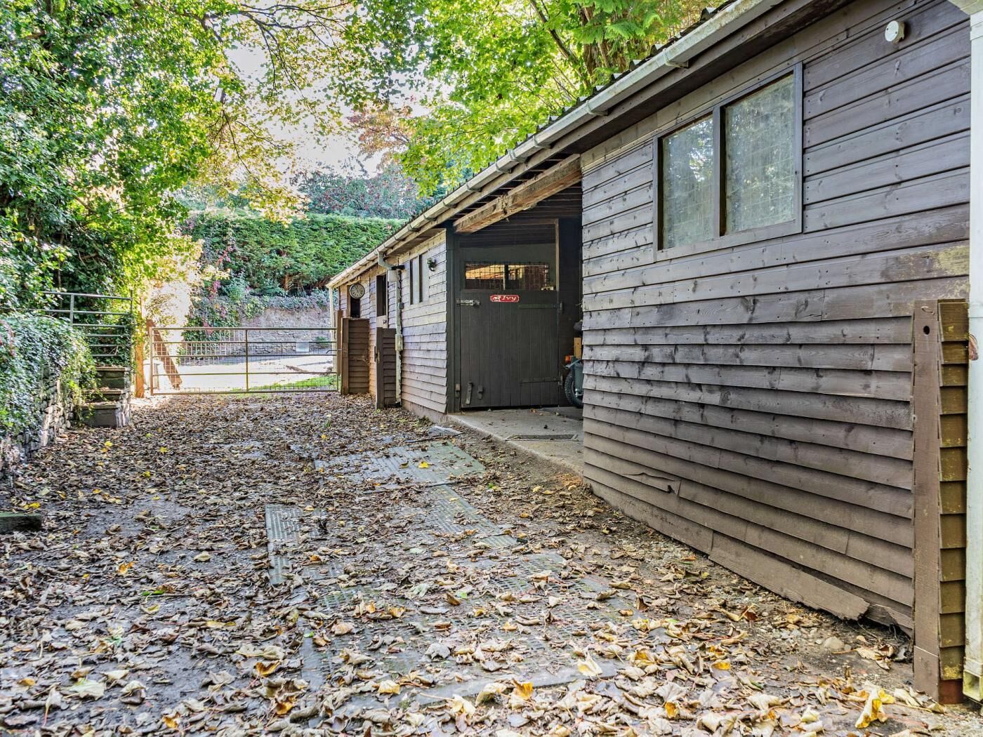 A wooden building with a covered outdoor area, a gate, and a paved path.