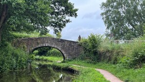 A stone bridge over a calm river, surrounded by lush greenery and a narrow path. - 1 Bed in Abergavenny (oc-52882) (Gilwern)