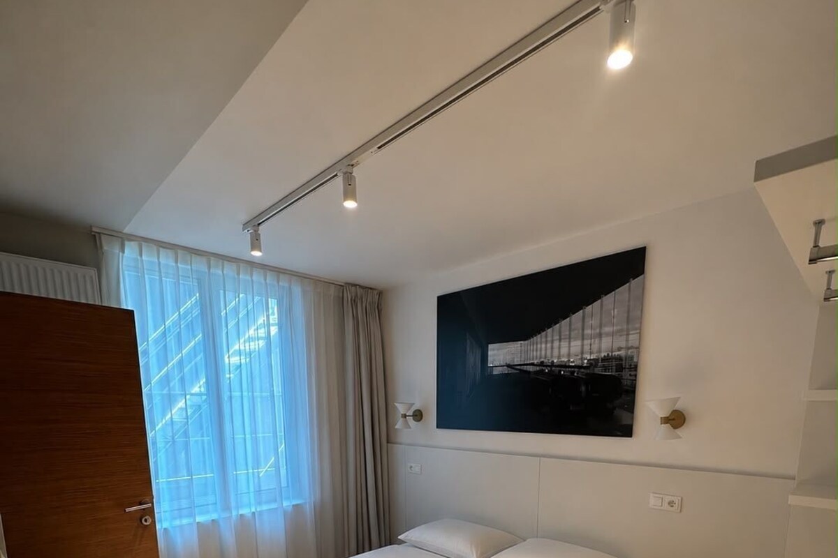 Ein modernes Hotelzimmer mit einem großen Bett, einem roten Akzentstuhl, einem Wandbild und einem Fenster mit transparenten Vorhängen.