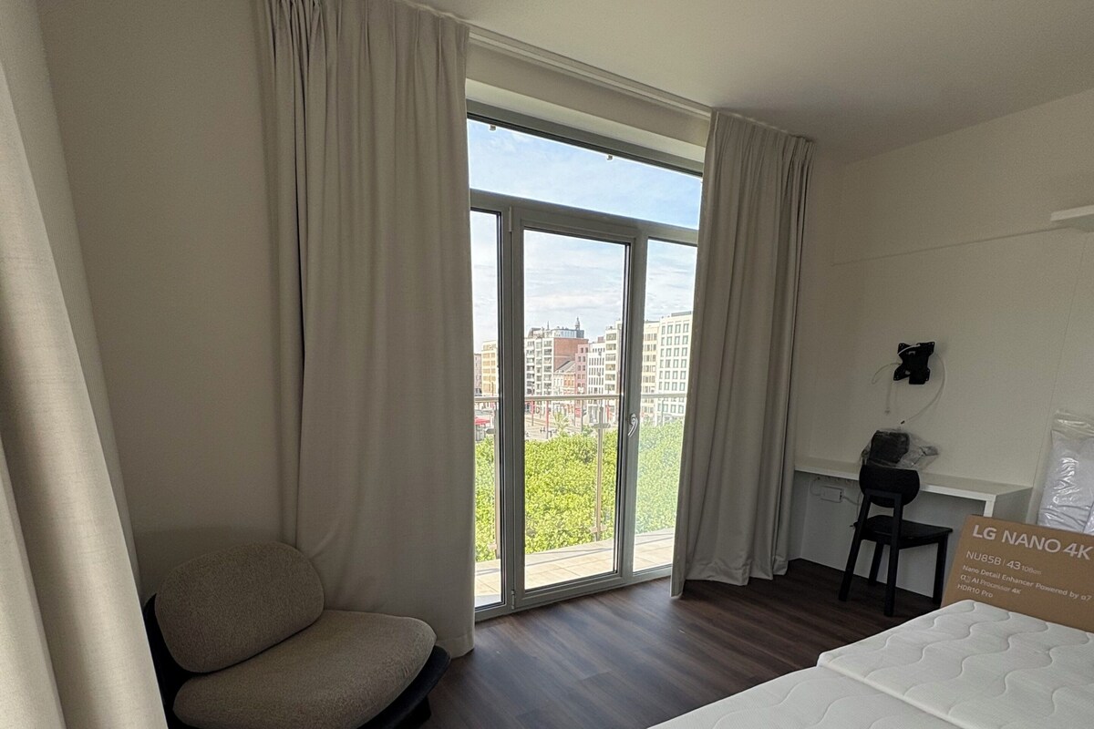 Ein Hotelzimmer mit Bett, Sessel, Schreibtisch und großem Fenster mit Blick auf die Stadt.
