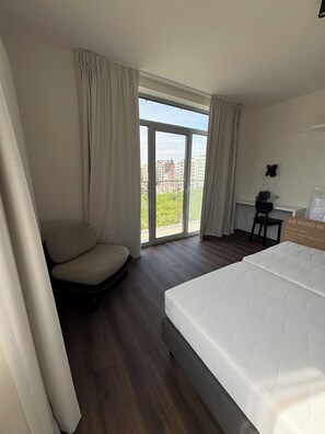 Ein Hotelzimmer mit Bett, Sessel, Schreibtisch und großem Fenster mit Blick auf die Stadt.