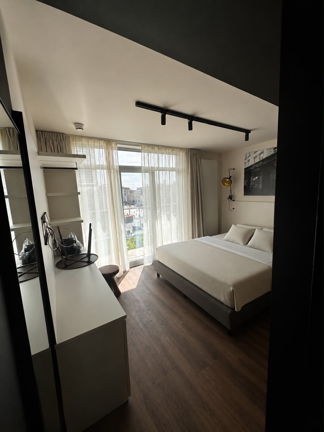A modern bedroom with a bed, a desk, and a large window.