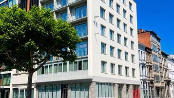 Un edificio moderno de varios pisos con fachada plana, ventanas amplias y un árbol en primer plano.