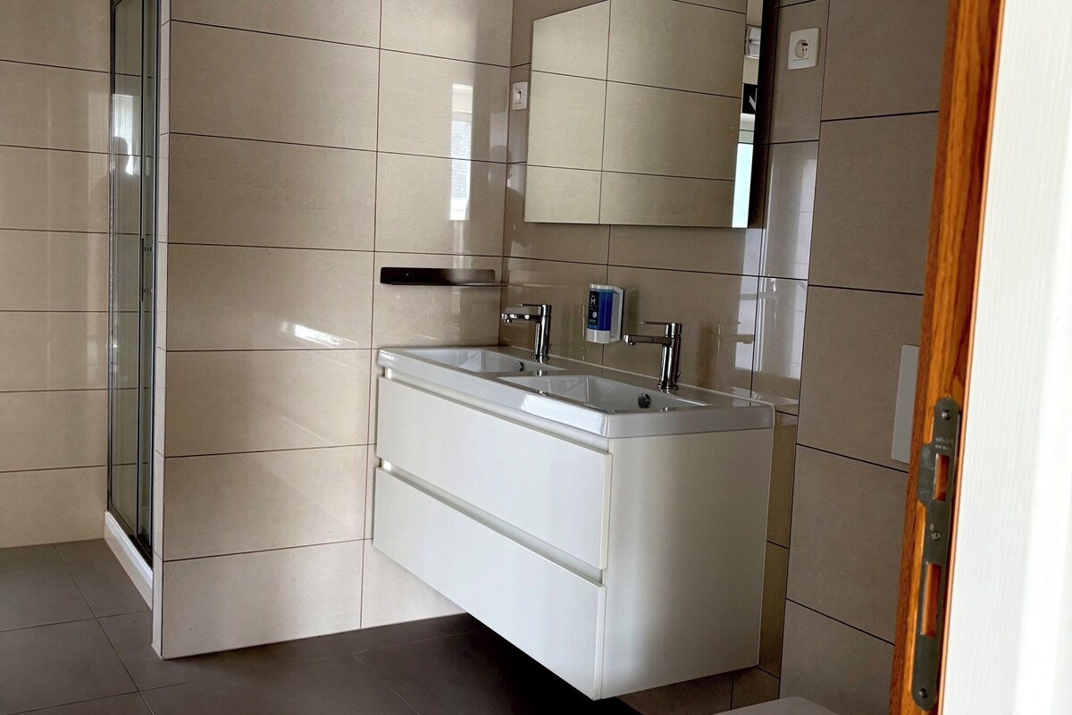 Un baño moderno con lavamanos en esquina, inodoro y cabina de ducha de vidrio.