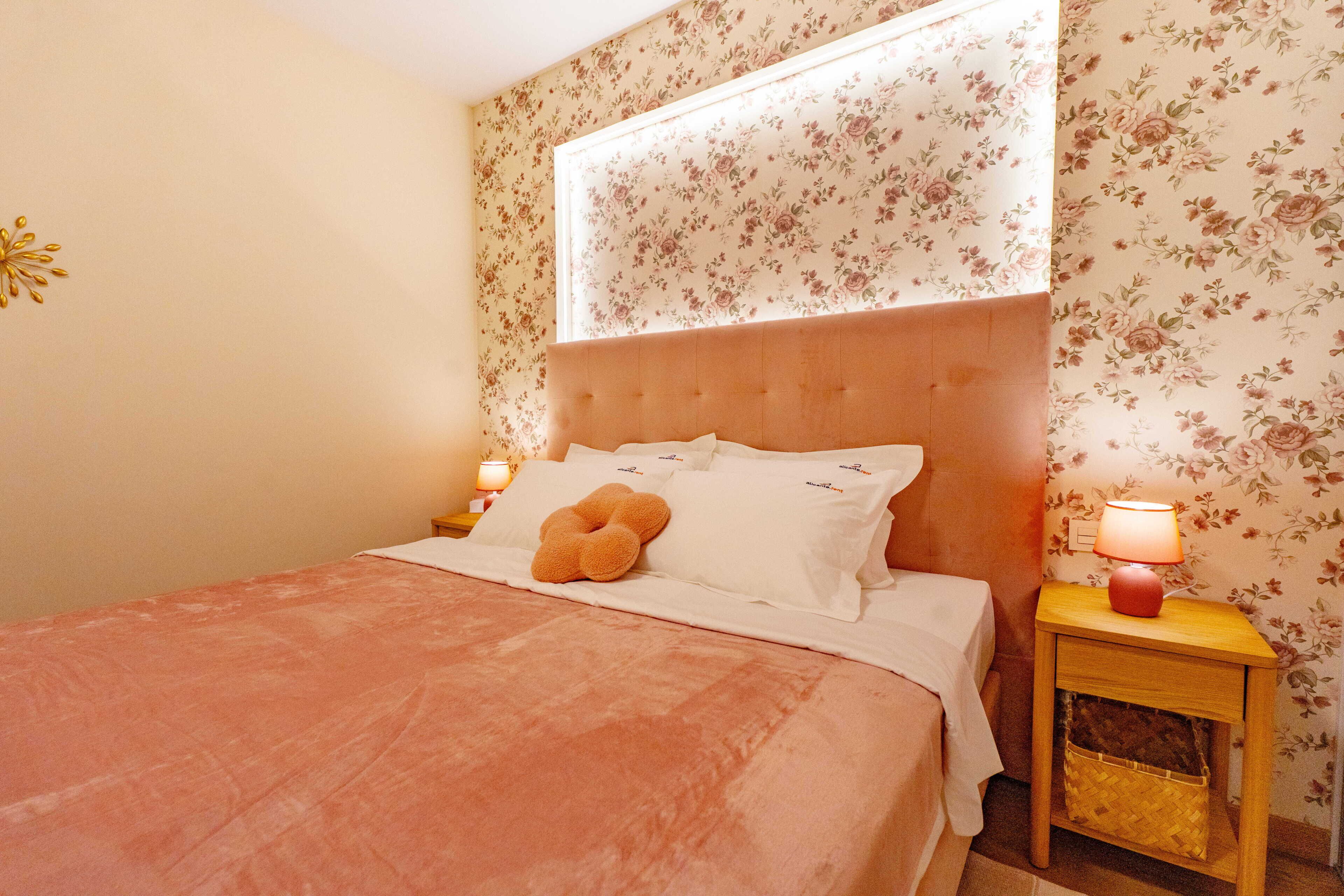Une chambre à coucher avec un lit, une table de chevet avec une lampe et un papier peint à motifs floraux.