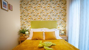 Un lit avec une couverture jaune et deux oreillers, une tête de lit verte et un mur orné d’un motif de feuilles.