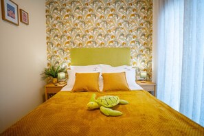 Ein Bett mit gelber Decke und zwei Kissen, ein grünes Kopfteil und eine Wand mit Blätermuster.