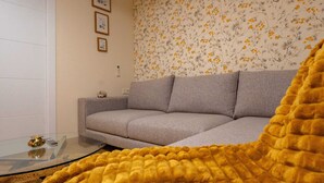 Un salon avec un canapé gris, une table basse en verre et un plaid jaune.