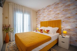 Hotelkamer met een bed, nachtkastje, lamp, vaas met bloemen en een raam met gordijnen.