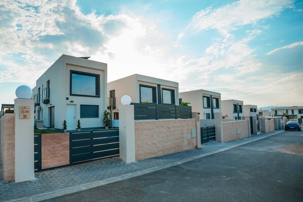 Een moderne villa met een hek, een verharde oprit en een heldere lucht.