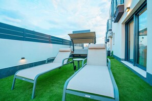 Un espace extérieur aménagé avec deux fauteuils et une table, entouré de gazon synthétique et bordé par la façade d’un bâtiment moderne.