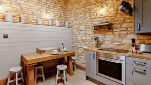 Uma cozinha com parede de pedra, mesa de madeira, banquetas, pia e forno embutido.