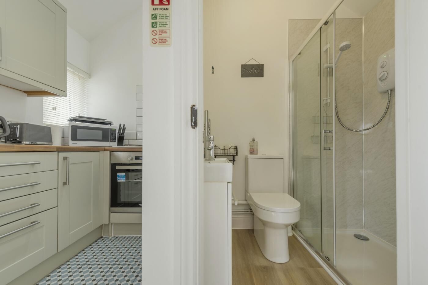 A compact kitchen with a microwave, toaster, and oven, a toilet with a shower, and a small sink.