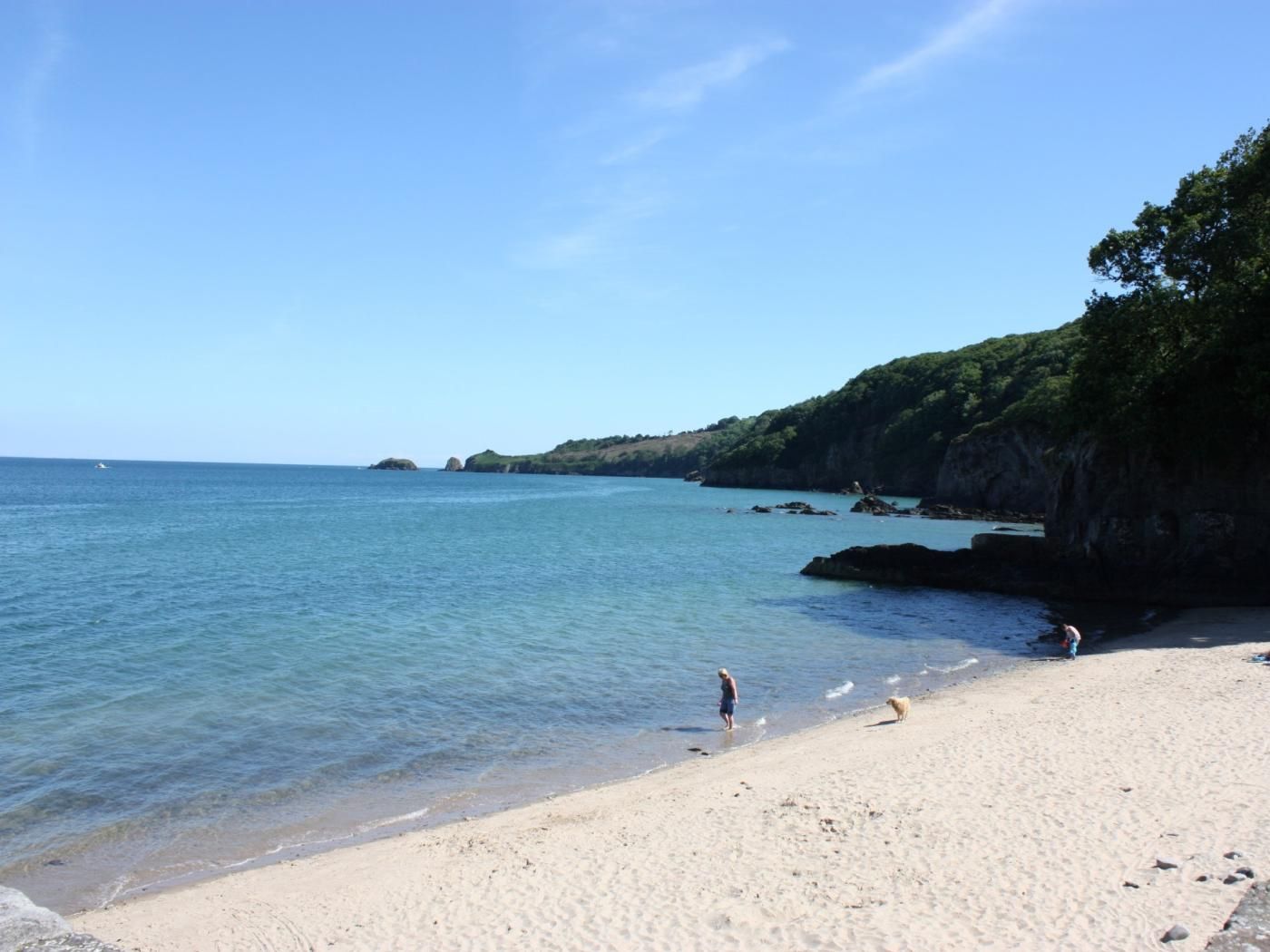 A beach with clear water, a sandy shore, and rocky cliffs.