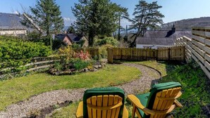 Ein Garten mit zwei Holz-Adirondack-Stühlen, einem Holzzaun und Blick auf Häuser und Bäume.