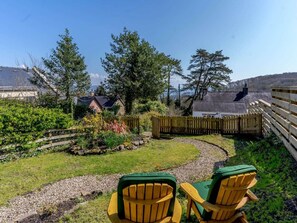 A garden with two wooden Adirondack chairs, a wooden fence, and a view of houses and trees. - 1 Bed in Saundersfoot (oc-52744) (Saundersfoot)