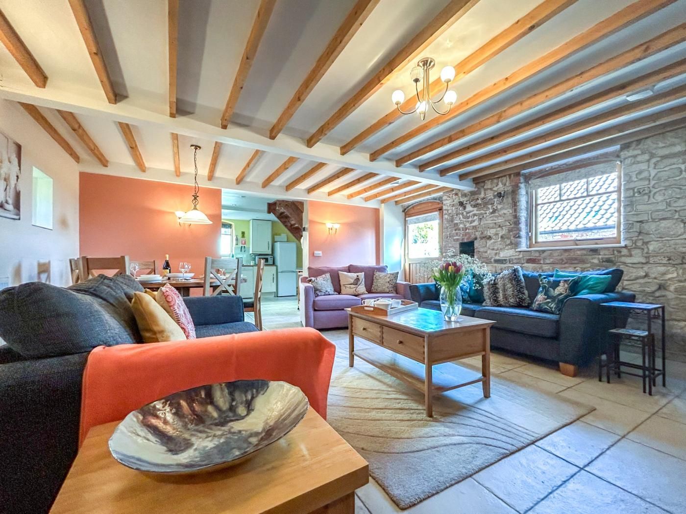 A spacious living area with a stone wall, wooden beams, and a mix of seating including a sofa, a loveseat, and a chair.