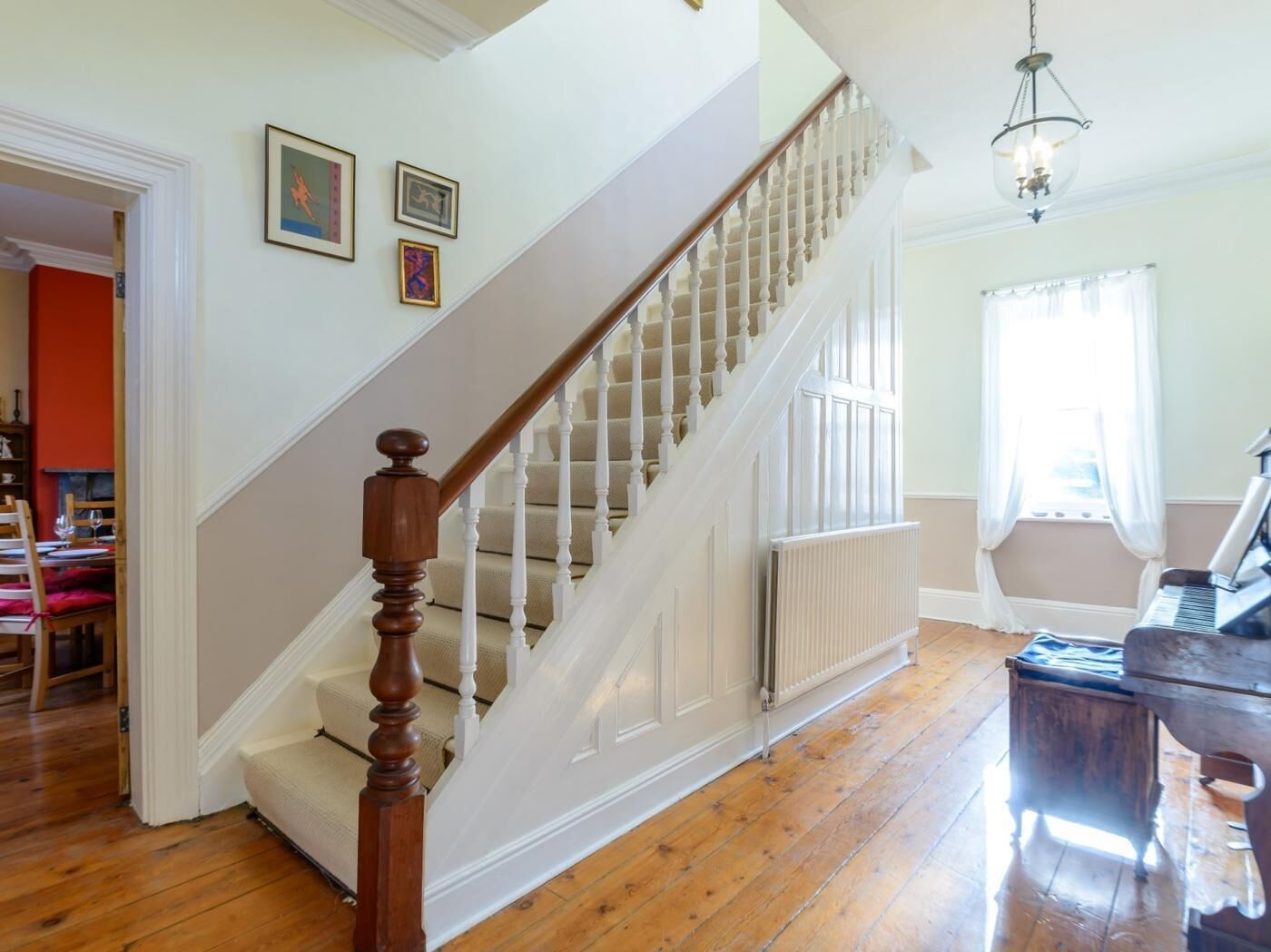 A staircase with a wooden handrail, a radiator, and a piano in a room with wooden flooring.