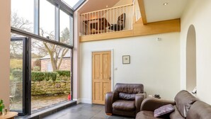 A spacious living area with a high ceiling, a large window, a wooden door, and a brown leather sofa.