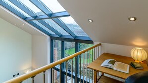 A modern room with a skylight, a wooden table with books, and a lamp.