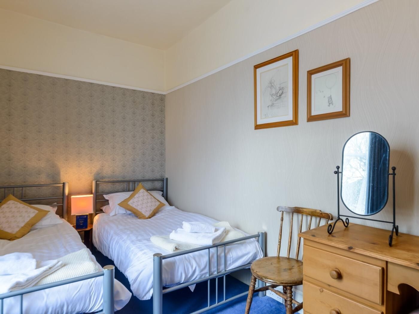 A bedroom with two beds, a wooden dresser, a chair, and two framed pictures on the wall.